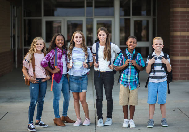 Large Group portrait of pre-adolescent school kids smiling in front of the school building. Back to school photo of a diverse group of children wearing backpacks and ready to go to school